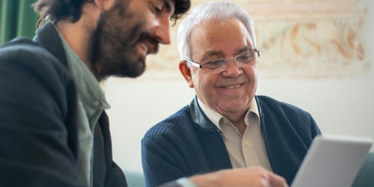 Image of younger man explaining something to an older man using a tablet.